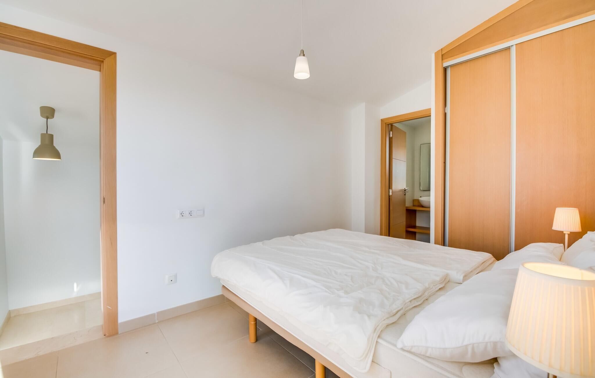 A bedroom with a bed, a bedside lamp, a wardrobe, and a door leading to a bathroom.