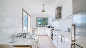 Una cocina moderna con armarios blancos, una mesa de comedor con sillas, una ventana y una lámpara colgante.