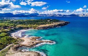 Vista aérea de una zona costera con aguas turquesas cristalinas, costas rocosas y montañas al fondo.