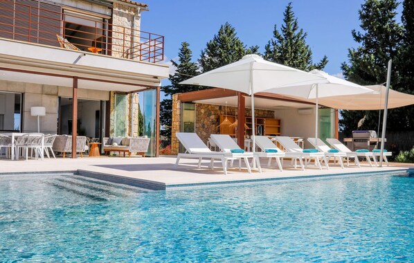 A modern pool area with lounge chairs and umbrellas, a stone facade, and a clear blue pool. - Cozy home in Costitx with private swimming pool, can be inside or outside (Costitx)