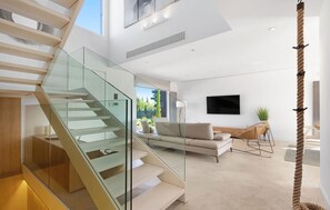 A modern living room with a glass staircase, a sofa, a TV, and a plant. - Cozy home in Costitx with private swimming pool, can be inside or outside (Costitx)