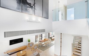 A spacious, modern interior with a high ceiling, a dining area with a wooden table and chairs, a seating area with a sofa and a coffee table, and a staircase leading to an upper level. - Cozy home in Costitx with private swimming pool, can be inside or outside (Costitx)