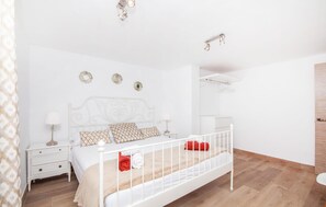 A bedroom with a white bed, a nightstand, a lamp, and a wall-mounted shelf. - Cozy home in Santa Maria with sauna (Santa Maria)