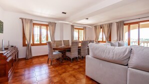 Ein geräumiges Wohnzimmer mit Holzboden, einer Essecke mit Korbstühlen und einem grauen Sofa.