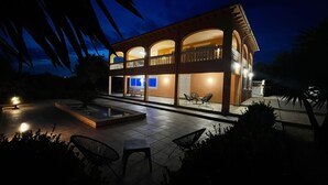 Ein modernes, zweistöckiges Haus mit Balkon, Schwimmbad und Sitzgelegenheit im Freien.