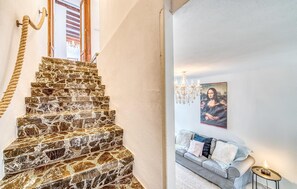 Eine Treppe mit Seilgeländer, einer Kristallleuchter und einem Gemälde einer Frau an der Wand.