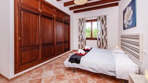 A bedroom with a large wooden wardrobe, a bed with towels, a window with patterned curtains, and a painting on the wall. - Lovely home in Binissalem with private swimming pool, can be inside or outside (Binissalem)