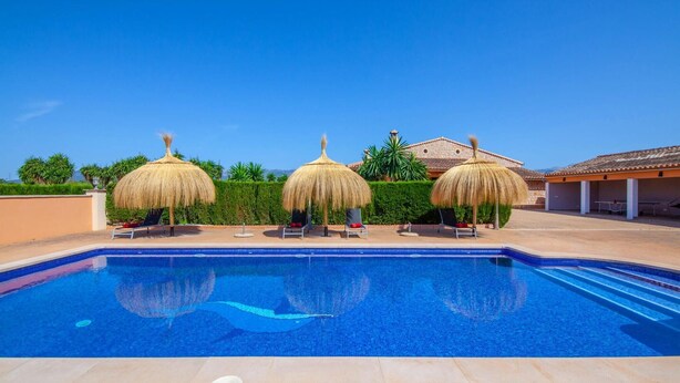 A swimming pool with three thatched umbrellas and lounge chairs, surrounded by a well-maintained hedge and a building with a tiled roof. - Lovely home in Binissalem with private swimming pool, can be inside or outside (Binissalem)
