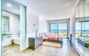 Une chambre moderne avec un grand lit, une douche en verre et un balcon offrant une vue sur la mer.