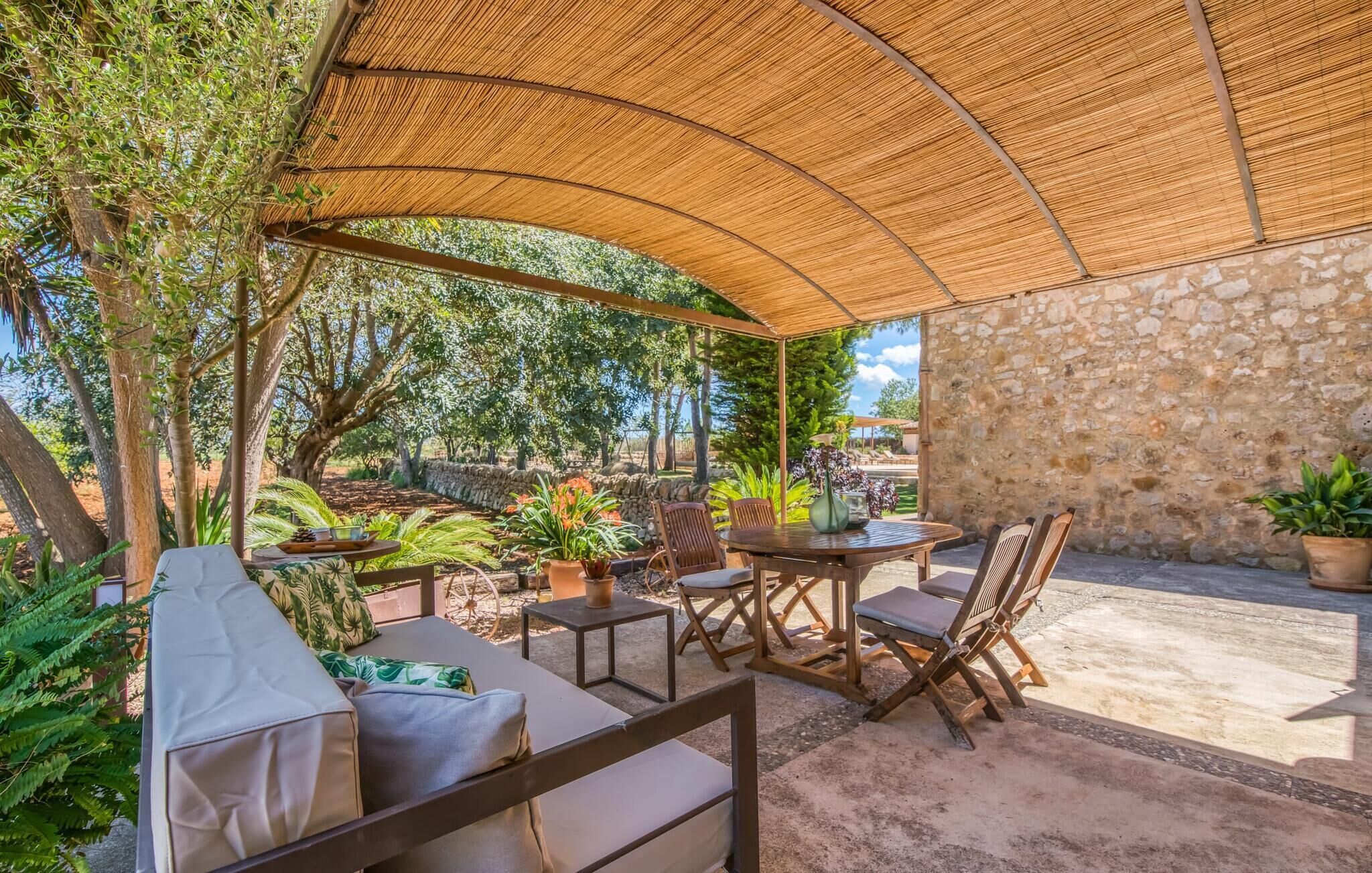 Une terrasse extérieure dotée d’un toit de chaume, d’un mur en pierre et d’un espace détente avec des coussins et des chaises.