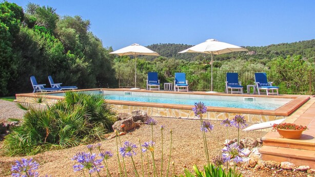 Ein Swimmingpool mit Liegestühlen und Sonnenschirmen, umgeben von viel Grün und Blumen.