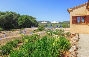 A garden with flowers and a building with red shutters. - Gorgeous home in Canyamel with private swimming pool, can be inside or outside (Canyamel)