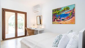 Ein Schlafzimmer mit Bett, Schreibtisch, Stuhl, einem Gemälde und Blick durch eine Glastür.