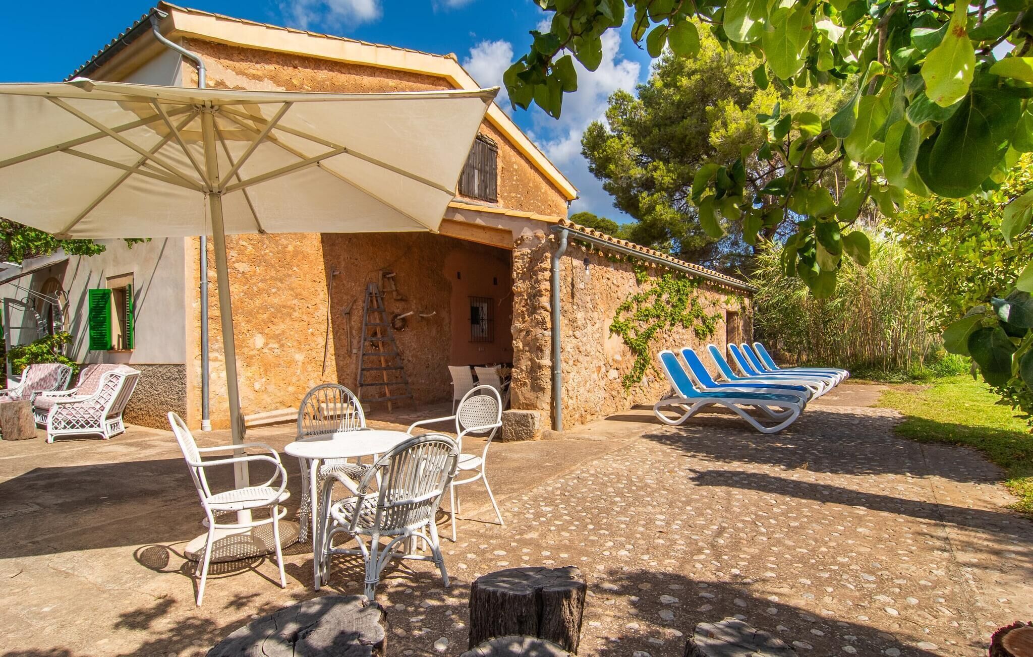Un área de estar al aire libre con encanto, que incluye una mesa, sillas, un porche cubierto y una fila de sillones de sol.
