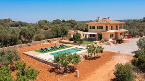 Eine zweistöckige Villa mit Pool, Sitzgelegenheiten im Freien und Blick auf die umliegende Landschaft.