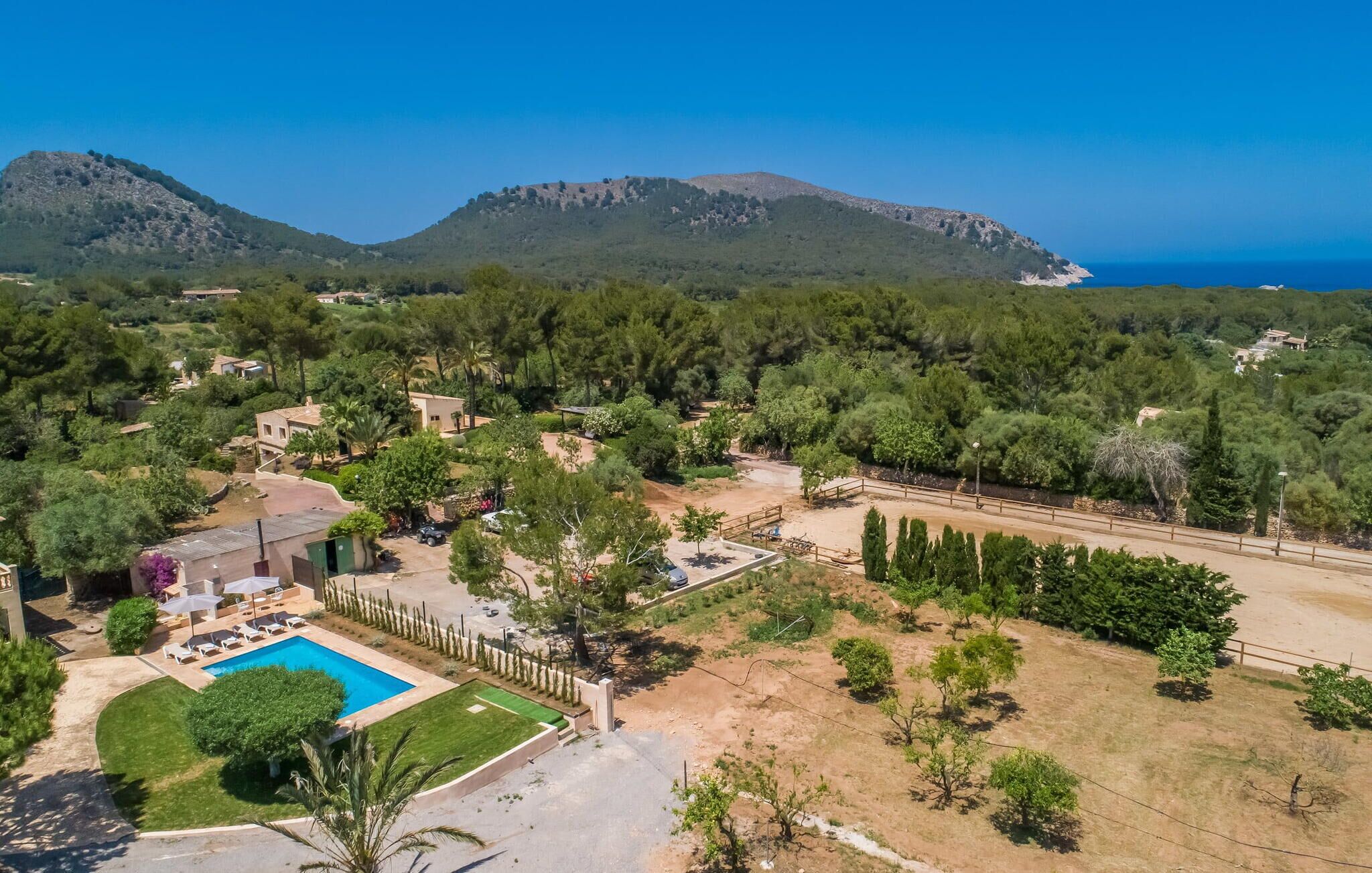 A residential area with a swimming pool, surrounded by trees and a view of the sea and mountains.