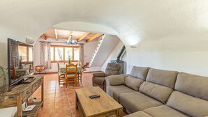 A cozy living room with a wooden sofa, a coffee table, and a dining area with a table and chairs. - Amazing home in Cala Ratjada (Cala Ratjada)
