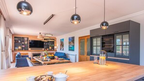 Una cucina moderna con isola in legno, illuminazione a sospensione e un'area pranzo con divano blu e tavolino da caffè.