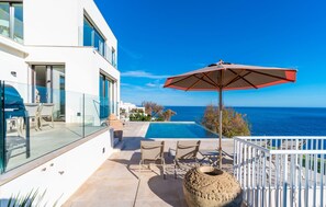 Ein modernes Gebäude mit einem Glasbalkon mit Blick auf einen Pool und das Meer.
