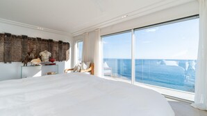 A spacious bedroom with a large bed, a glass desk with decorative items, and a view of the ocean through floor-to-ceiling windows. - Awesome home in Porto Cristo (Porto Cristo)