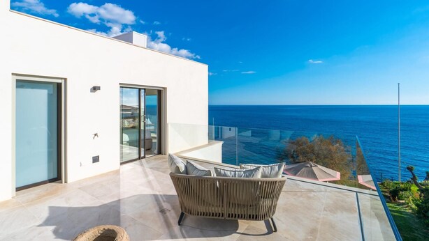 A modern outdoor balcony with a view of the sea, a wicker sofa, and a glass door. - Awesome home in Porto Cristo (Porto Cristo)