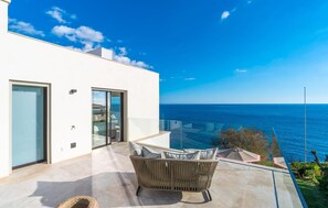 Ein moderner Balkon im Freien mit Meerblick, einer Rattan-Couch und einer Glastür.