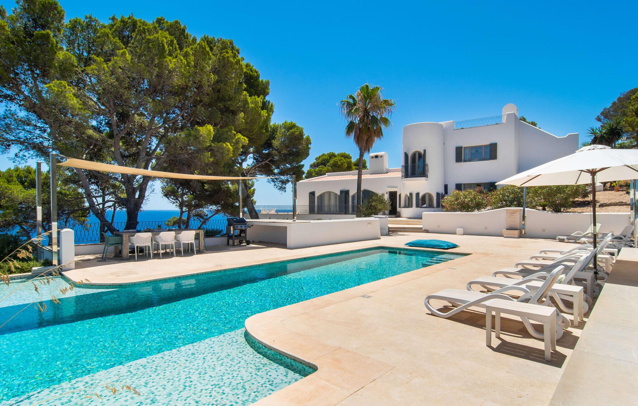 Ein Poolbereich mit Liegestühlen, einem Grill und Blick aufs Meer.