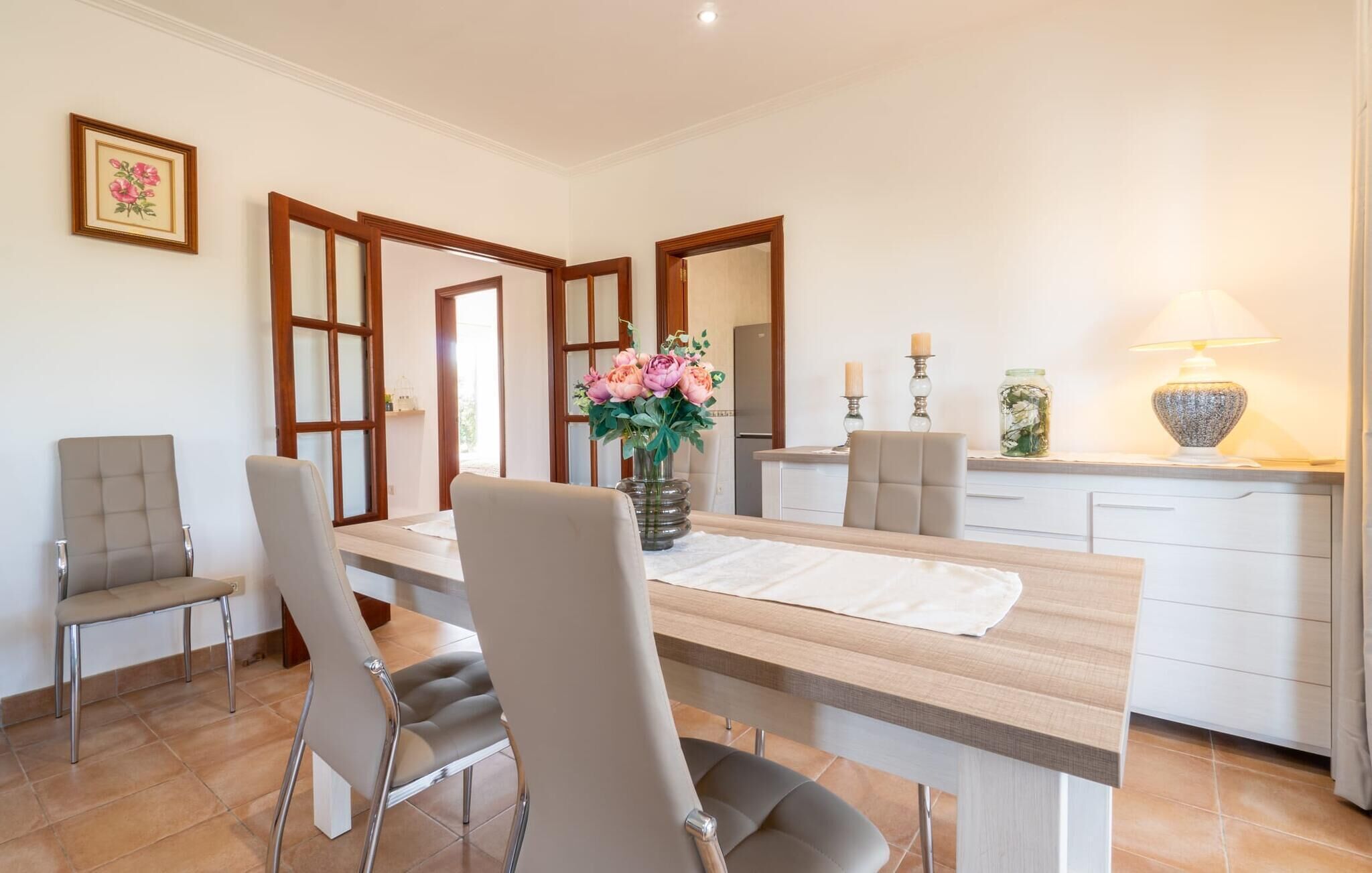 Un coin repas avec une table en bois, quatre chaises, un vase de fleurs et, au fond, une cuisine.