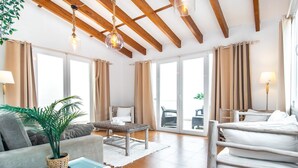 Ein geräumiges Zimmer mit hoher Decke, großen Fenstern, einem Bett, einer Couch, einem Esstisch und einer Topfpflanze.