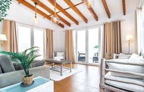 Ein geräumiges Zimmer mit hoher Decke, großen Fenstern, einem Bett, einer Couch, einem Esstisch und einer Topfpflanze.