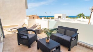 Eine Dachterrasse mit Korbmöbeln, einem Blumentopf und Blick aufs Meer.