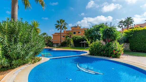 Una piscina con una fuente de agua azul cristalina, rodeada de exuberante vegetación y un edificio de varios pisos al fondo.