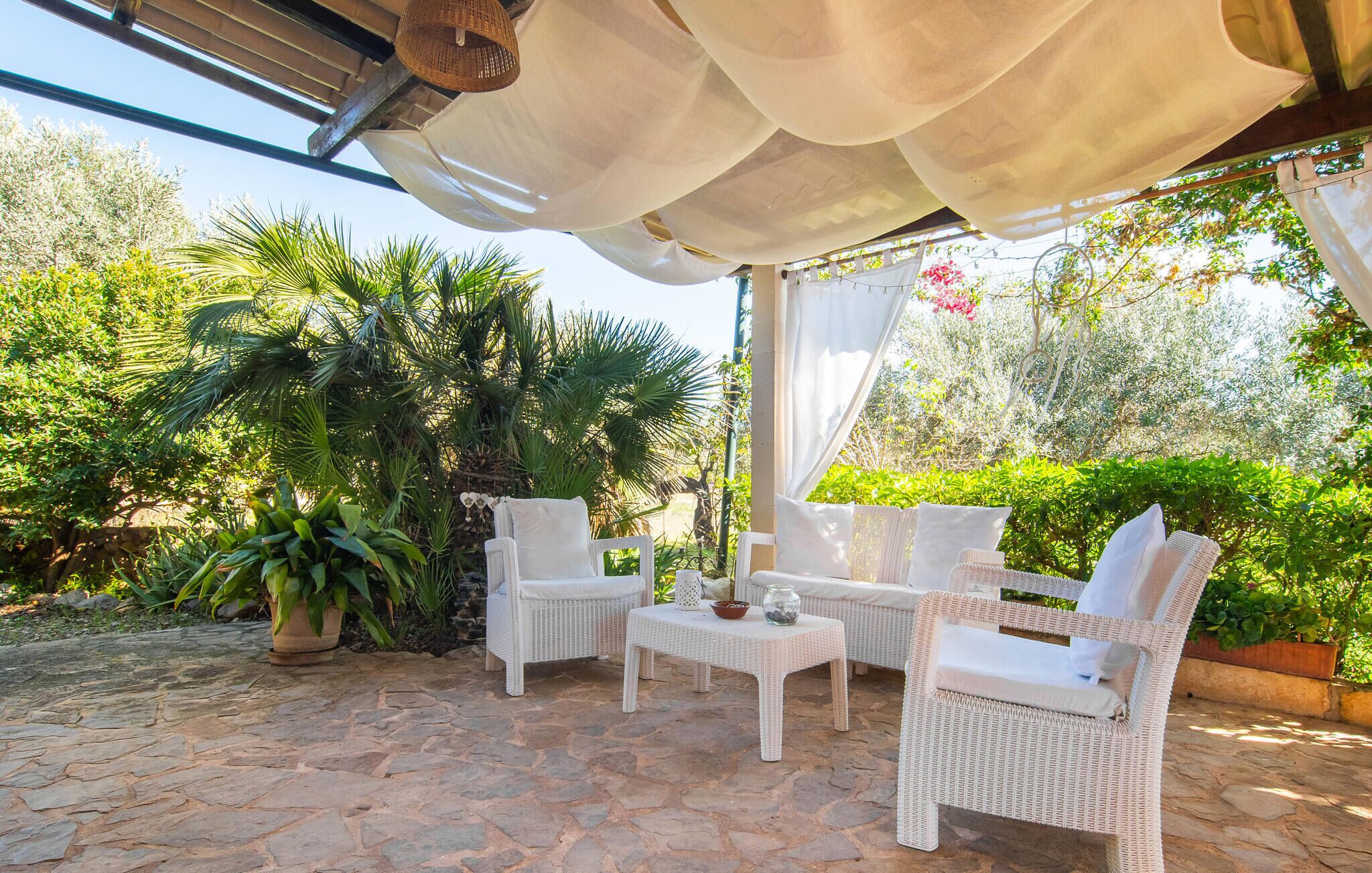 Un patio al aire libre con muebles de mimbre, suelo de piedra y abundante vegetación.