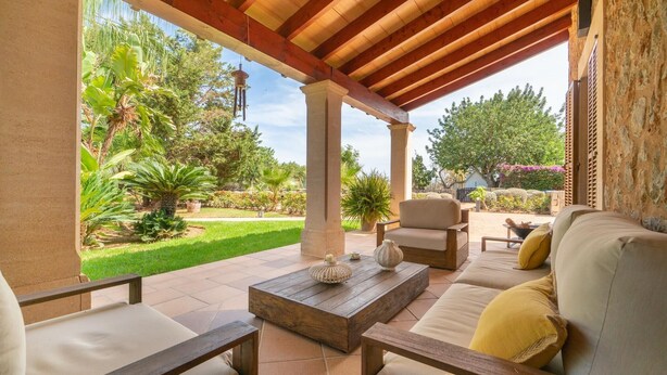 Eine Terrasse im Freien mit einer Holz-Pergola, einem Sofa, zwei Stühlen und einem Couchtisch.