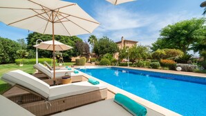 Ein Poolbereich mit Liegestühlen, einem großen Sonnenschirm und einem gepflegten Garten.