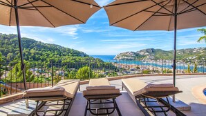 A terrace with three lounge chairs and two large umbrellas, overlooking a coastal landscape with hills and a sea view. - Lovely home in Port d'Andratx with sauna (Port d'Andratx)