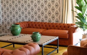 Una habitación con un sofá naranja con capitoné, una mesa de centro de madera y un papel tapiz estampado.