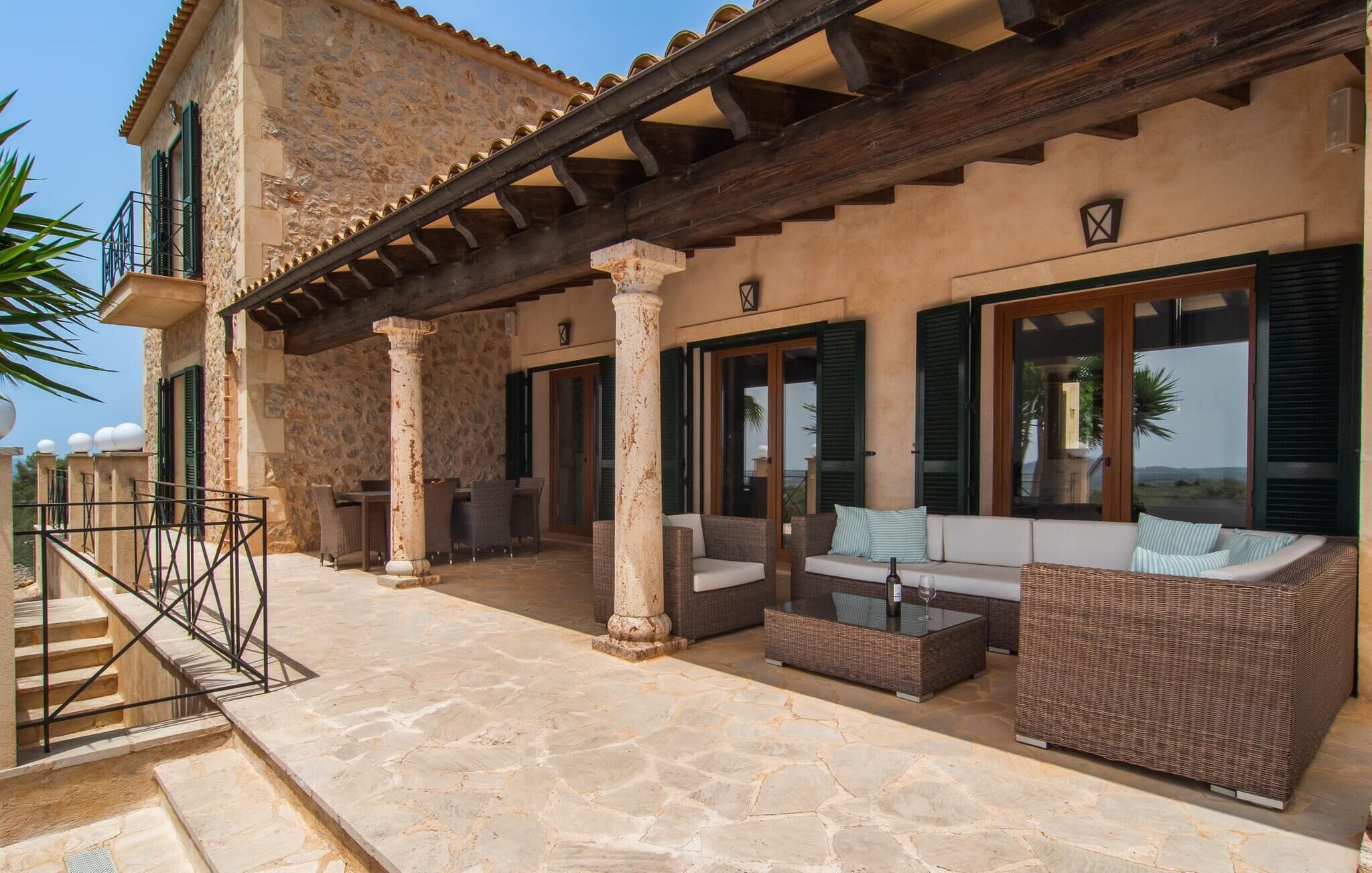 Un edificio de piedra con terraza, columnas y una pérgola.