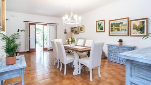 A dining area with a wooden table, white chairs, and a chandelier. There are framed paintings on the wall and a potted plant on the table. - 3 bedroom gorgeous home in Alcudia (Alcudia)