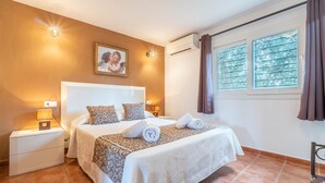 Een slaapkamer met een groot bed, twee nachtkastjes, een wandairconditioner en een raam met gordijnen.
