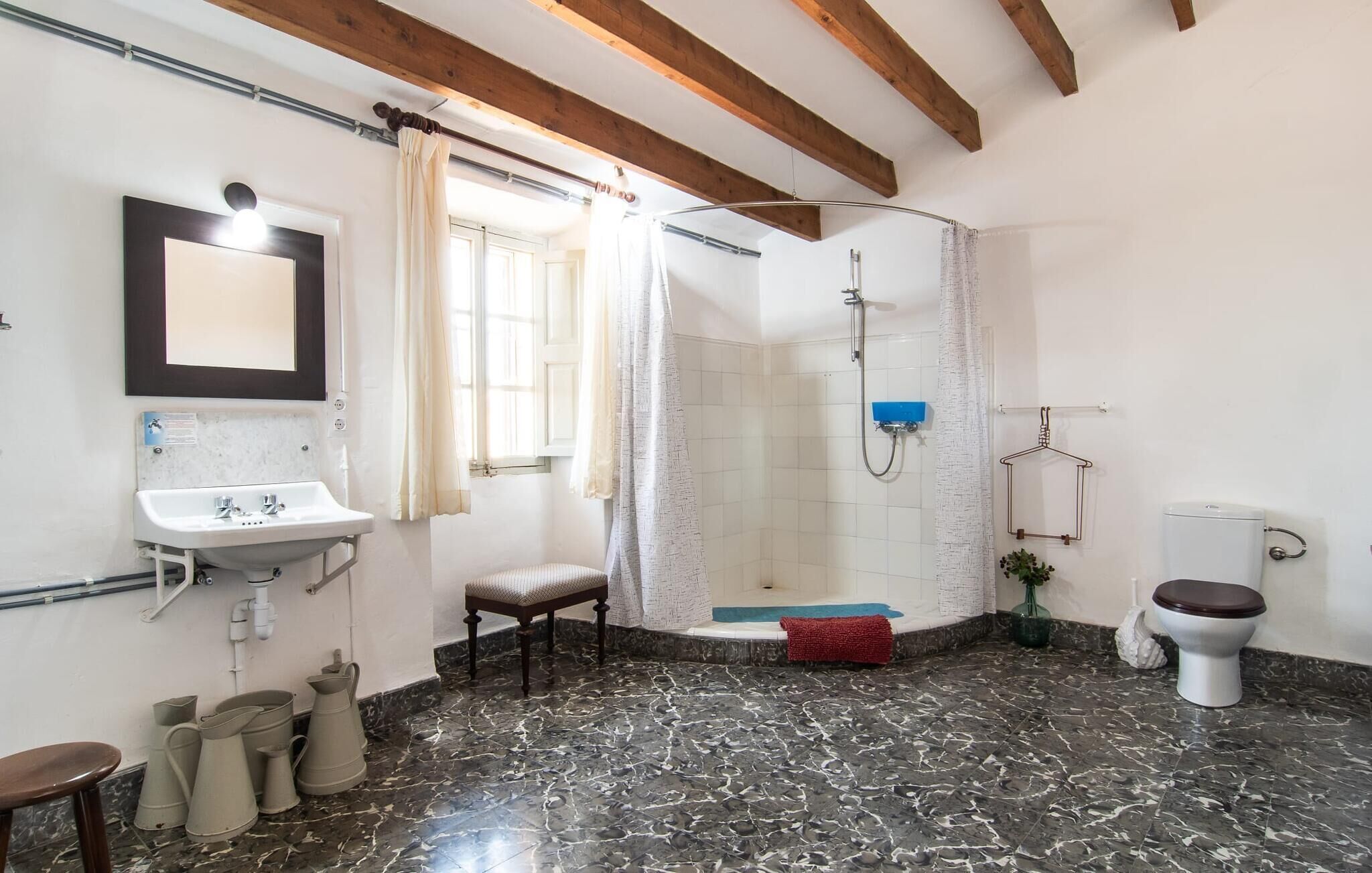 A bathroom with a sink, toilet, shower, and a chair.
