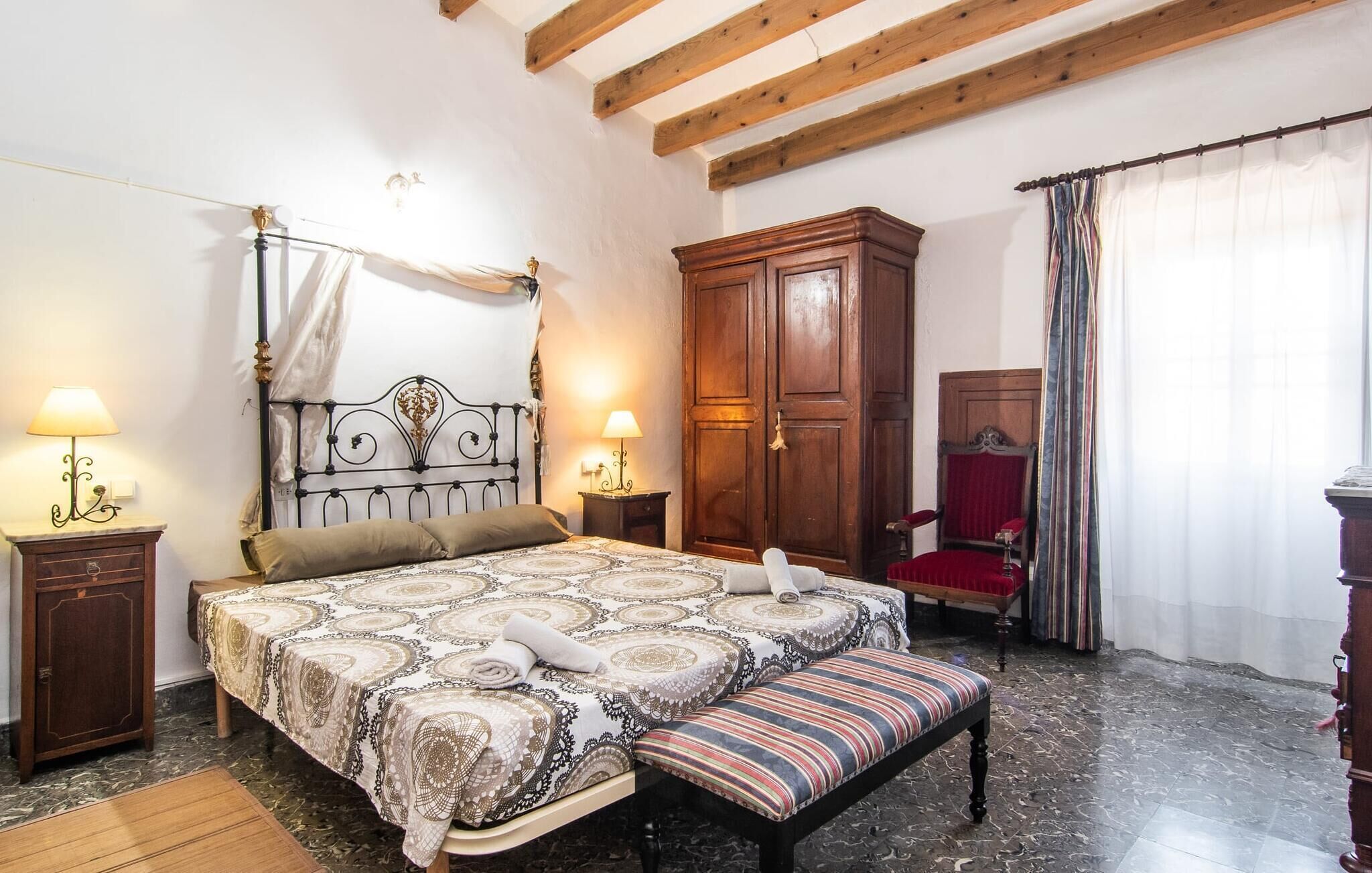 Une chambre à coucher avec un lit à baldaquin, une armoire en bois, un fauteuil rouge et un banc.