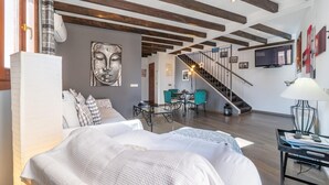 Sala moderna com vigas de madeira aparentes, uma cama grande, área de jantar com cadeiras verde-água e uma escada.