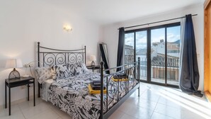 Une chambre à coucher moderne, avec un lit, des tables de chevet, un miroir et une vue sur la ville grâce à de grandes fenêtres.