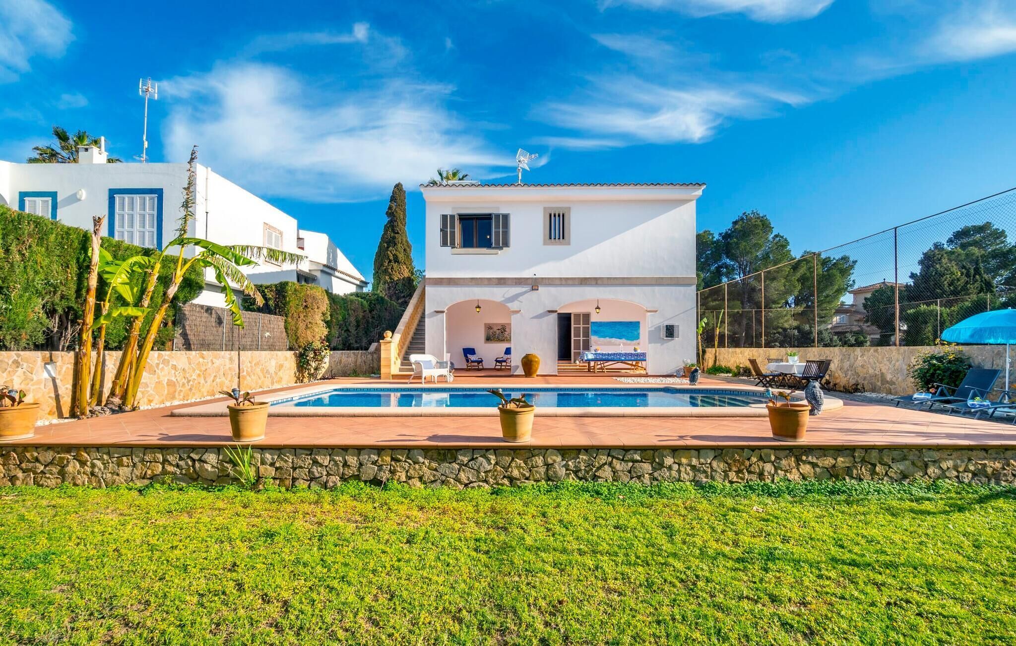 Una villa moderna con piscina, mobiliario de exterior y un muro de piedra.