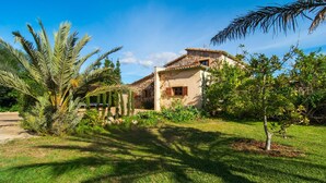 A house with a stone facade, a tiled roof, and a well-maintained garden with palm trees and shrubs. - Beautiful home in Pollenca with private swimming pool, can be inside or outside (Pollenca)