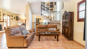 A spacious living room with a brown leather sofa, a wooden coffee table, and a staircase leading to an upper floor. - Beautiful home in Pollenca with private swimming pool, can be inside or outside (Pollenca)