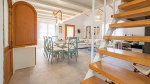 Ampla sala de estar com mesa de jantar, cadeiras e escada com degraus de madeira.
