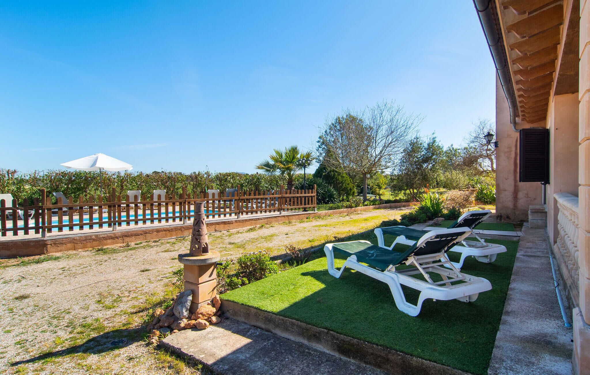 A poolside area with lounge chairs, a small fountain, and a view of a pool and trees.
