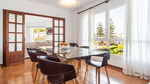 A dining area with a glass table, six chairs, a bowl of fruit, and a view of trees through large windows. - Amazing home in Porto Cristo (Porto Cristo)